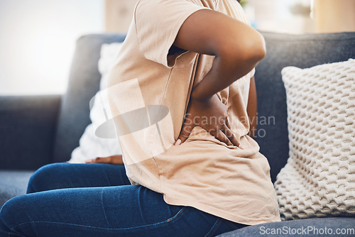 Image of Woman with a back injury, pain or accident from stress sitting on sofa in her living room. Black girl with a muscle sprain, back pain or injured spine medical emergency on couch in lounge at home.