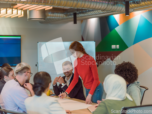 Image of A diverse team of business experts in a modern glass office, attentively listening to a colleague's presentation, fostering collaboration and innovation