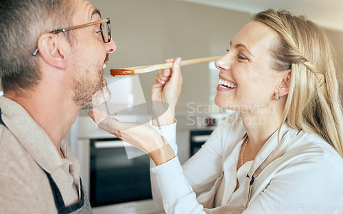 Image of Cooking woman feed man to taste food, meal and lunch in kitchen at home. Happy, smile and care wife giving, hungry and tasting husband mouth spoon of tomato sauce while couple eating dinner with love