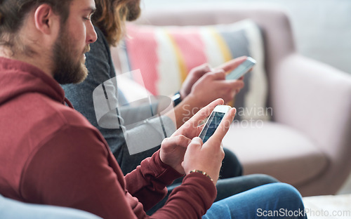 Image of Young man using smartphone browsing social media texting messages sitting on sofa with friend