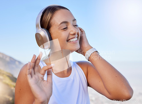 Image of Music streaming, fitness headphones and web radio of a woman athlete listening to a song in nature. Happy smile after a workout on the mountain with blue sky and happiness relax hearing a track