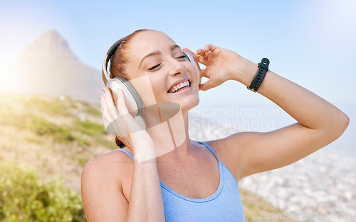 Image of Fitness, nature and a woman with headphones listening to music with smile and mountain background. Exercise, streaming app and a workout playlist online. Summer sky, sun and happy training with song.