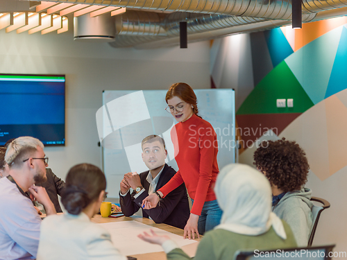 Image of A diverse team of business experts in a modern glass office, attentively listening to a colleague's presentation, fostering collaboration and innovation