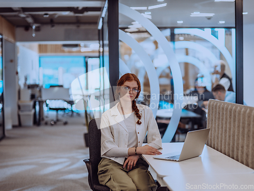 Image of A young businesswoman with orange hair sitting confidently, fully engaged in her work on the laptop, exuding creativity, ambition, and a vibrant sense of individuality