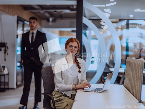Image of A young businesswoman with orange hair sitting confidently, fully engaged in her work on the laptop, exuding creativity, ambition, and a vibrant sense of individuality