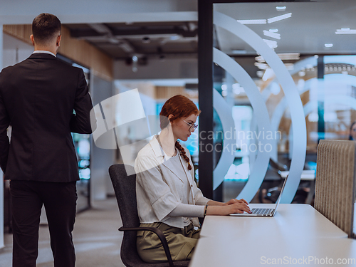 Image of A young businesswoman with orange hair sitting confidently, fully engaged in her work on the laptop, exuding creativity, ambition, and a vibrant sense of individuality