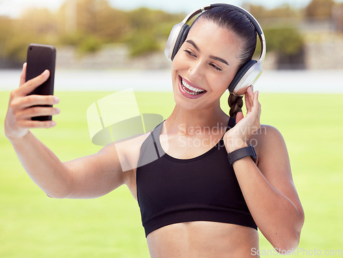 Image of Phone, woman and fitness influencer taking a selfie at training, running and workout outdoors on sports racetrack. Smile, healthy and happy girl in headphones sharing fitness journey on social media