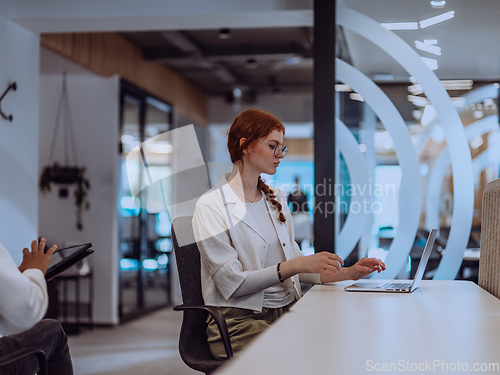 Image of A young businesswoman with orange hair sitting confidently, fully engaged in her work on the laptop, exuding creativity, ambition, and a vibrant sense of individuality