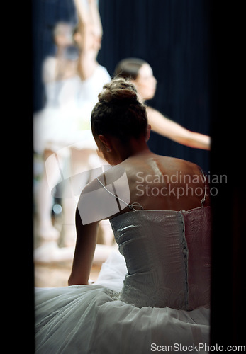 Image of A ballerina backstage of a performance at a theatre on stage. Ballet dancer sitting on the floor while play or concert is happening. She is getting ready, doing warm up and preparing to dance