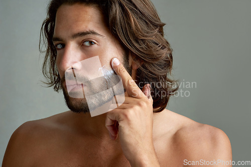 Image of Portrait, facial or lotion with a shirtless man in studio on a gray background for his grooming routine. Skincare, face and beauty with the body of a young person with antiaging cream for his skin