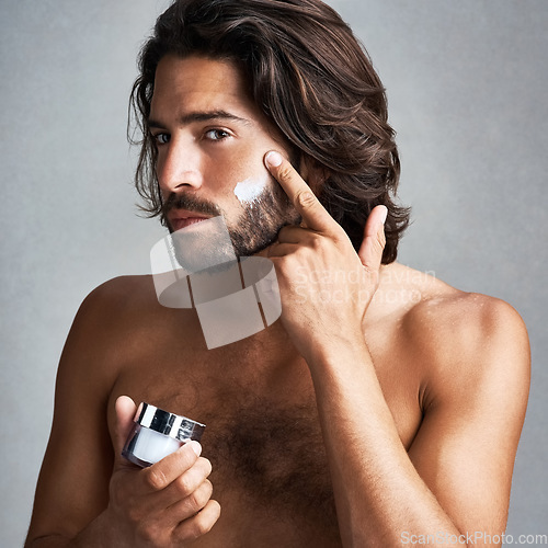 Image of Portrait, skincare or cream with a shirtless man in studio on a gray background for his grooming routine. Beauty, facial and and the body of a handsome young person with antiaging lotion for his skin