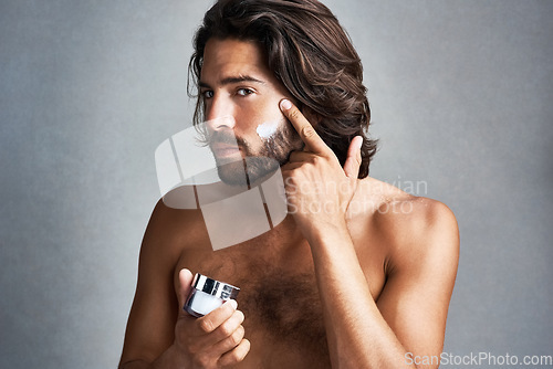Image of Portrait, skincare or lotion with the face of a man in studio on a gray background for his grooming routine. Beauty, facial and a handsome or shirtless young person with antiaging cream for his skin