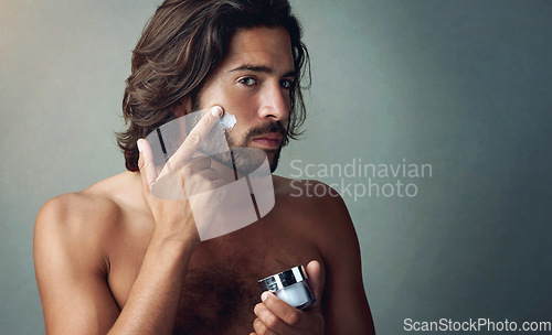 Image of Portrait, skincare or lotion with a shirtless man in studio on a gray background for his grooming routine. Beauty, facial and and the body of a handsome young person with antiaging cream for his skin