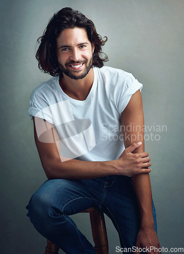 Image of Fashion, smile and portrait of man in studio on a stool with casual, cool and stylish outfit. Happy, handsome and confident young male model from Mexico with trendy style on chair by gray background.