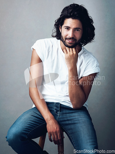 Image of Fashion, handsome and portrait of man in studio on a stool with casual, cool and stylish outfit. Happy, smile and confident young male model from Mexico with trendy style on chair by gray background.