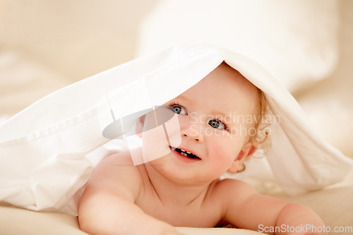 Image of Smile, face and happy baby on a bed with blanket for playing, games or fun in a nursery room. Learning, child development and curious little boy kid in a bedroom with sheet cover while lying in house