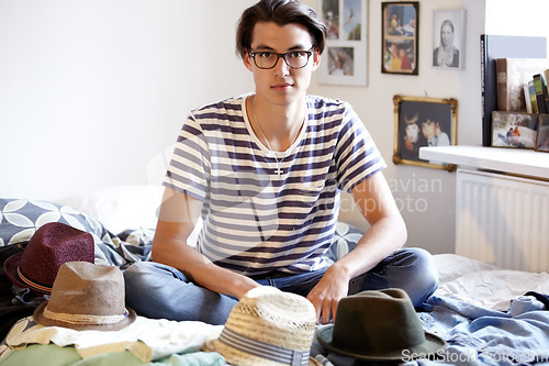 Image of Fashion, hats and portrait of man in bedroom with fedora collection in home and apartment with nerd. Geek, style and person on bed with choice of vintage hat with trendy glasses and planning outfit