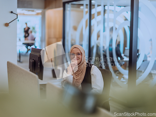 Image of In a modern office, a young Muslim entrepreneur wearing a hijab sits confidently and diligently works on her computer, embodying determination, creativity, and empowerment in the business world