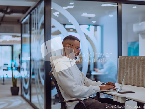 Image of In a modern office setting, an African American businessman is diligently working on his laptop, embodying determination, ambition, and productivity in his professional environmen