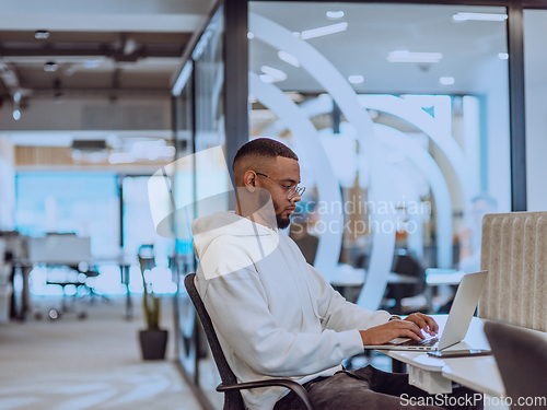Image of In a modern office setting, an African American businessman is diligently working on his laptop, embodying determination, ambition, and productivity in his professional environmen