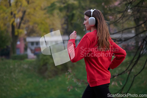 Image of Young beautiful woman running in autumn park and listening to music with headphones on smartphone