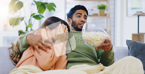 Image of Fear, jump and couple watching tv on a sofa with popcorn for movie, film or streaming show at home. Omg, television and people hug in living room with cinema snack for scary, horror or spooky series