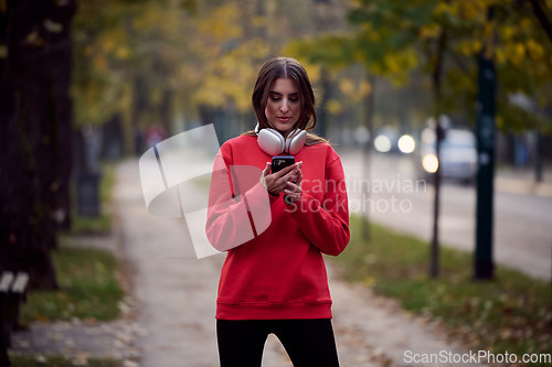 Image of Sporty woman checks smartphone before doing some exercises listens music from a playlist