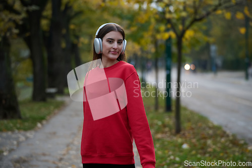 Image of Portrait of running woman after jogging in the park on autumn seasson. Female fitness model training outside on a cozy fall day and listening to music over smartphone.
