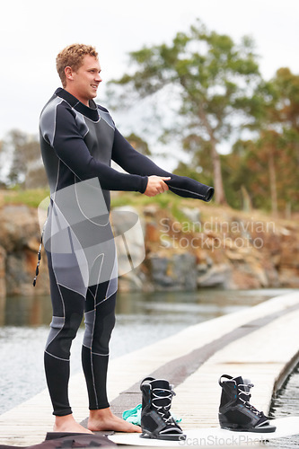 Image of Sports, wetsuit and man by lake with wakeboard for surfing, exercise and recreation hobby outdoors. Fitness, extreme sport and person with board for water skiing for freedom, adventure and fun