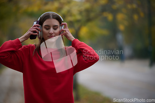 Image of Portrait of running woman after jogging in the park on autumn seasson. Female fitness model training outside on a cozy fall day and listening to music over smartphone.