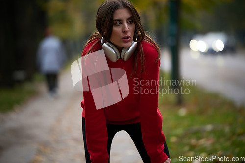 Image of Athletic young woman taking a breath and relaxing after jogging and stretching. Woman Training and Workout Exercises On Street.