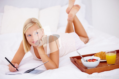 Image of Woman, bed and notebook with breakfast, happy and writing in diary, thinking and bedroom for journaling. Food, fruits and croissant with orange juice, nutrition or healthy diet in home, rest or relax
