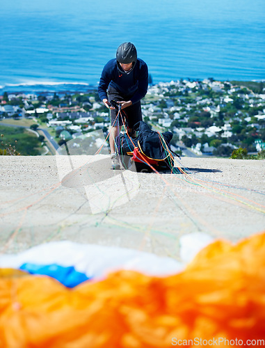 Image of Man, parachute and paragliding sport in launch on hill, healthy adventure and extreme fitness by ocean. Person, preparation and fearless by bench for flight with helmet and safety gear by blue sky