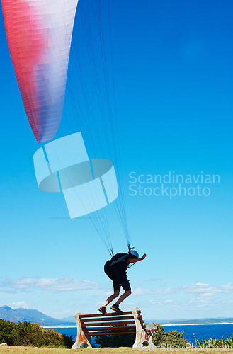 Image of Man, parachute or paragliding sport in launch exercise, healthy adventure or extreme fitness for wellness. Person, preparation and fearless by bench for flight with helmet and safety gear by blue sky