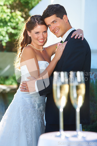 Image of Happy couple, portrait and hug at wedding with champagne glasses in celebration for love, commitment or marriage. Man hugging woman for embrace, affection or support with alcohol at outdoor ceremony