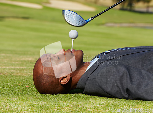 Image of Black man, face and lying on golf course with tee in mouth for hole in one on green grass or field. African male person, golfer or assistant holding ball with club hovering for swing or hit on pitch