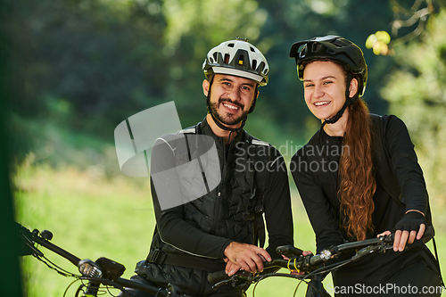 Image of A blissful couple, adorned in professional cycling gear, enjoys a romantic bicycle ride through a park, surrounded by modern natural attractions, radiating love and happiness