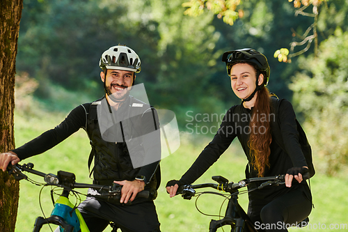 Image of A blissful couple, adorned in professional cycling gear, enjoys a romantic bicycle ride through a park, surrounded by modern natural attractions, radiating love and happiness