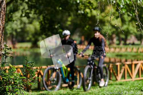 Image of A blissful couple, adorned in professional cycling gear, enjoys a romantic bicycle ride through a park, surrounded by modern natural attractions, radiating love and happiness