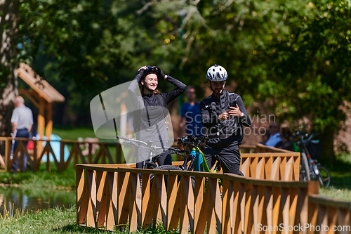 Image of A blissful couple, adorned in professional cycling gear, enjoys a romantic bicycle ride through a park, surrounded by modern natural attractions, radiating love and happiness