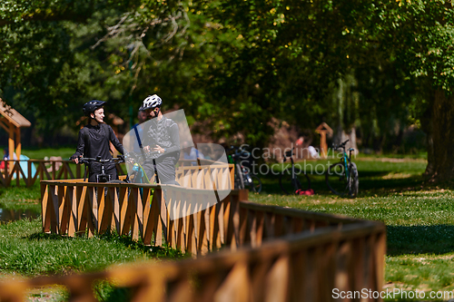 Image of A blissful couple, adorned in professional cycling gear, enjoys a romantic bicycle ride through a park, surrounded by modern natural attractions, radiating love and happiness