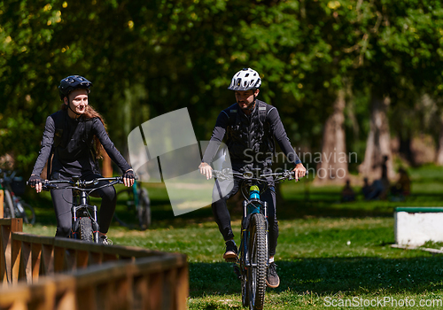 Image of A blissful couple, adorned in professional cycling gear, enjoys a romantic bicycle ride through a park, surrounded by modern natural attractions, radiating love and happiness