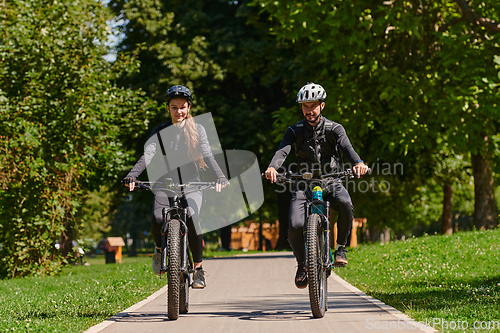 Image of A blissful couple, adorned in professional cycling gear, enjoys a romantic bicycle ride through a park, surrounded by modern natural attractions, radiating love and happiness