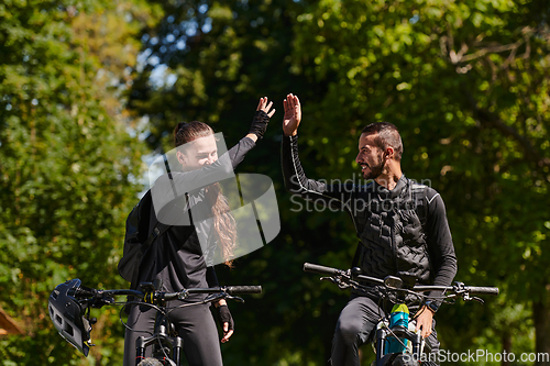 Image of A blissful couple, adorned in professional cycling gear, enjoys a romantic bicycle ride through a park, surrounded by modern natural attractions, radiating love and happiness