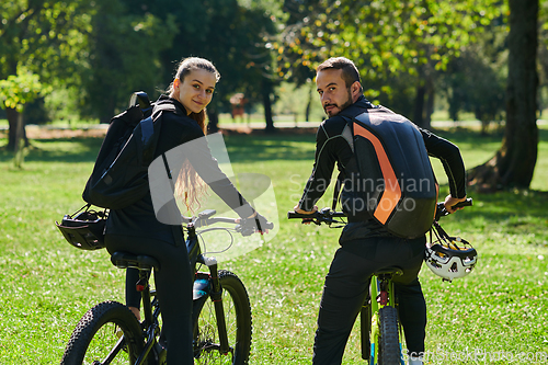 Image of A blissful couple, adorned in professional cycling gear, enjoys a romantic bicycle ride through a park, surrounded by modern natural attractions, radiating love and happiness