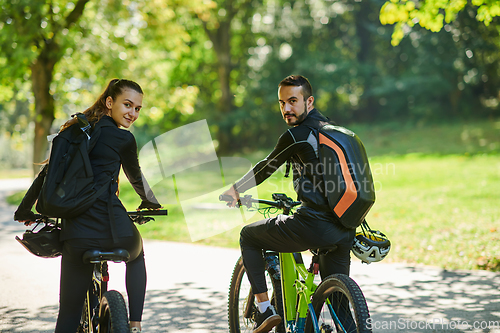 Image of A blissful couple, adorned in professional cycling gear, enjoys a romantic bicycle ride through a park, surrounded by modern natural attractions, radiating love and happiness