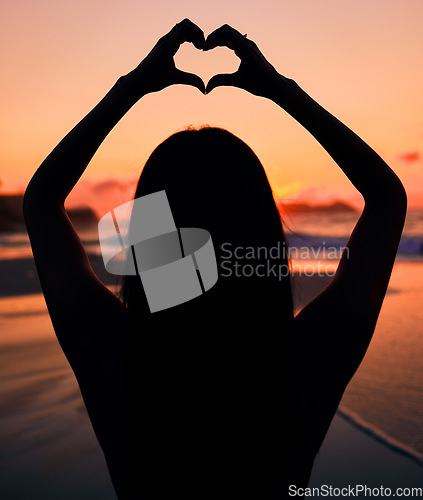 Image of Woman, silhouette and sunset by sea with heart hands for love, care and kindness with sign, summer and dusk. Girl, person and ocean with symbol, emoji or icon on vacation, beach and outdoor in dark