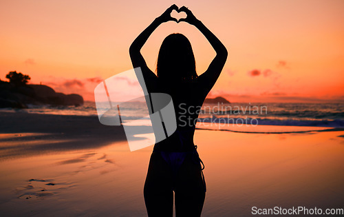 Image of Woman, silhouette and sunset by water with heart hands for love, care and kindness with sign, summer and body. Girl, person and beach with symbol, emoji or icon on vacation, ocean or outdoor at dusk