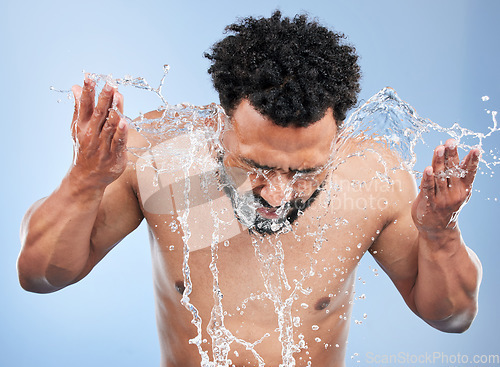 Image of Black man, water splash and face wash for skincare, hygiene or grooming against a blue studio background. African male person, model and aqua for body hydration, shower or facial skin treatment