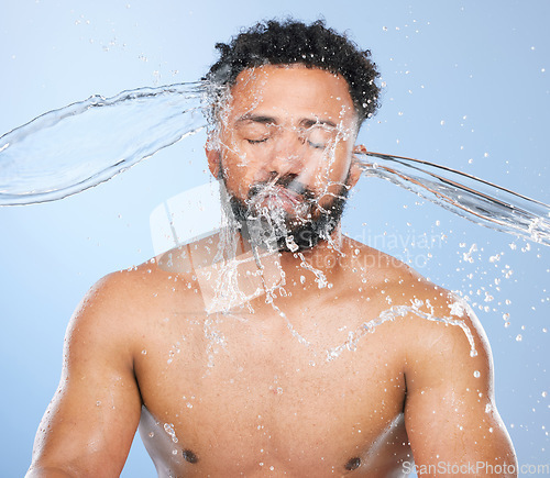Image of Black man, water splash and washing in skincare for cleaning, hygiene or grooming against a blue studio background. Face of African male person, model and aqua for body hydration, shower or skin wash